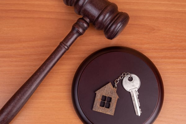 Wooden gavel and dark bowl containing a small wooden house and silver key on orange wood surface