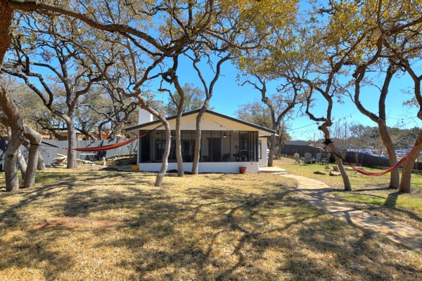 Single-story cottage with tan awning nestled among large oak trees, red hammocks visible in yard