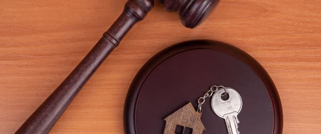 Wooden gavel and dark bowl containing small wooden house and silver key on orange wood surface