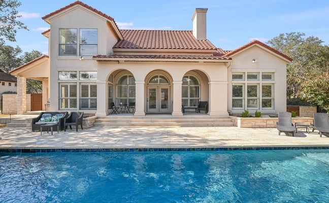 Modern Mediterranean-style house with arched windows, terracotta tile roof, and swimming pool in foreground