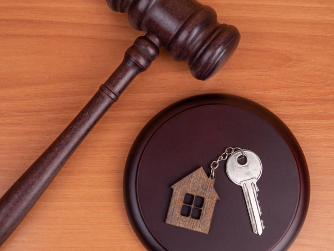 Wooden gavel and dark bowl containing a small wooden house figurine and silver key on orange wood surface