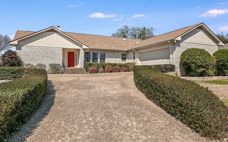 A charming front exterior of a home with a vibrant red door, attached garage, and a beautifully landscaped garden with flowering plants and shrubs