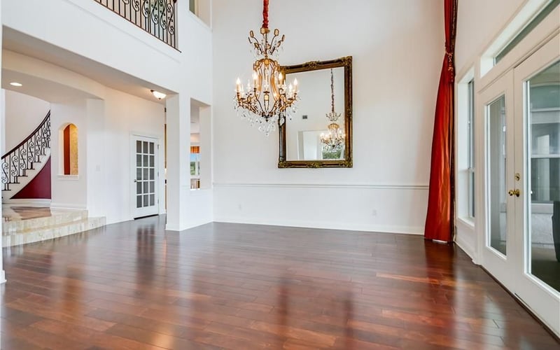 Spacious two-story foyer with hardwood floors, crystal chandelier, ornate mirror, and red curtains