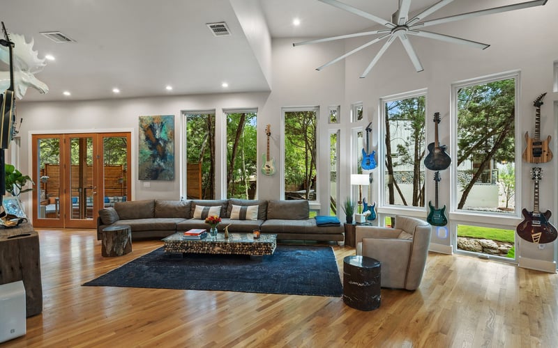 A bright and airy luxury living room with glass windows , featuring a neutral-colored sofa and armchair set,  coffee table, and woven area rug.
