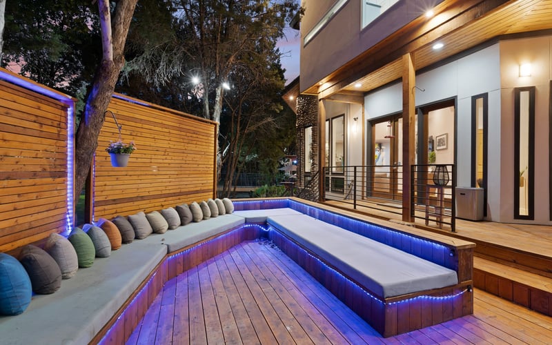 Stylish backyard with a wooden deck and outdoor sofa furniture, surrounded by lush greenery and decorated with potted plants and lights