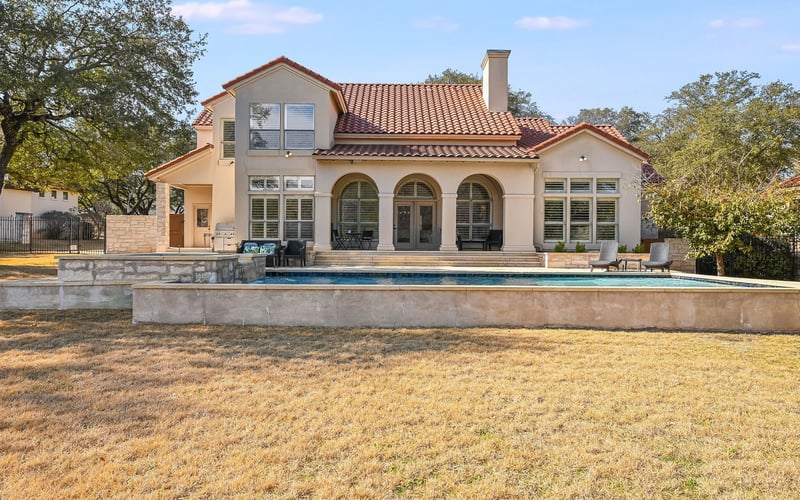 Modern Mediterranean-style house with terracotta tile roof, arched windows, and swimming pool overlooking manicured lawn.