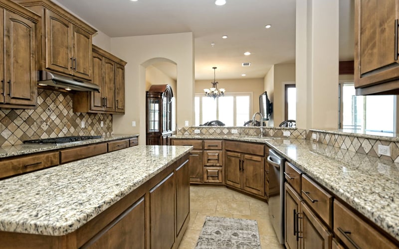 Large kitchen with wood cabinetry, granite countertops, diamond tile backsplash, and island seating overlooking open living area