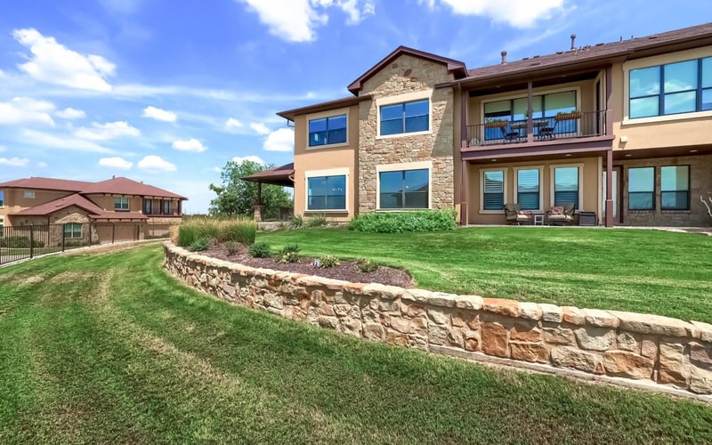 Modern two-story home with stone and stucco exterior, large windows, covered patio, and manicured lawn with stone retaining wall.