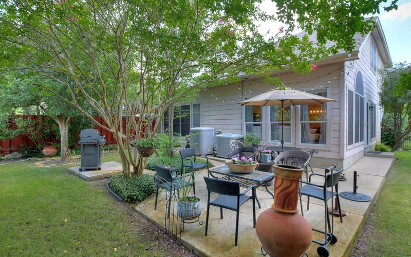 Backyard patio with seating area, umbrella, fire pit, and modern house under flowering trees